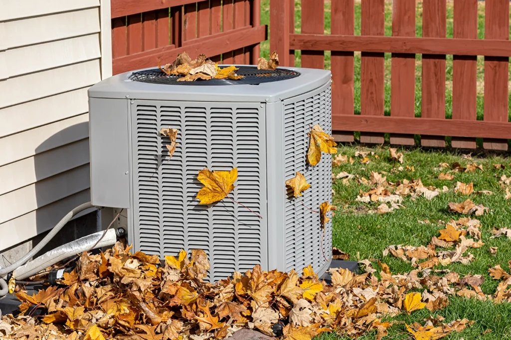 Outdoor HVAC unit covered in fall leaves, showing why an HVAC maintenance checklist is important for airflow and seasonal care.