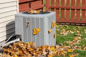 Outdoor HVAC unit covered in fall leaves, showing why an HVAC maintenance checklist is important for airflow and seasonal care.
