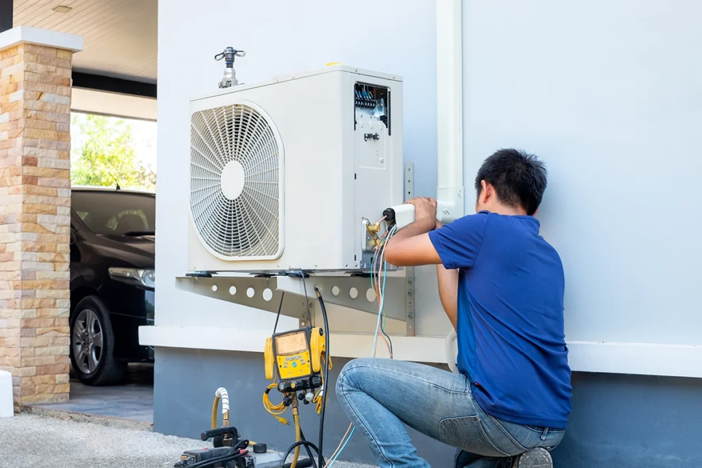 Technician performing heat pump maintenance on an outdoor unit using diagnostic tools